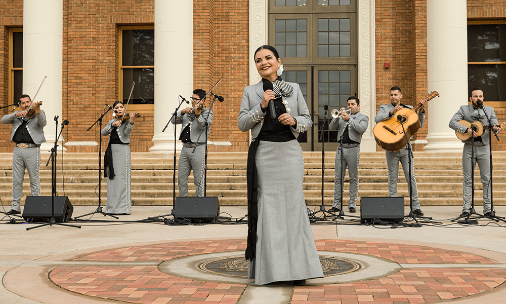 Image of Mariachi Voces Tapatias Band playing a variety of instruments in front of City Hall with singing in the foreground
